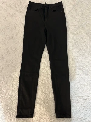 Svarta skinny jeans från Vero Moda - Svarta skinny jeans med klassisk femficksdesign och hög midja i Strl: S/30. Jeansen har smal passform hela vägen ner och är tillverkade i ett stretchigt material för extra komfort. 