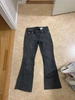 Grå bootcut jeans från True religion  - Säljer ett par gråa bootcut jeans från Ture religion med klassiska fem fickor och snygga detaljer på bakfickorna. Jeansen har låg midja och utsvängda ben, perfekta för en avslappnad och trendig look.