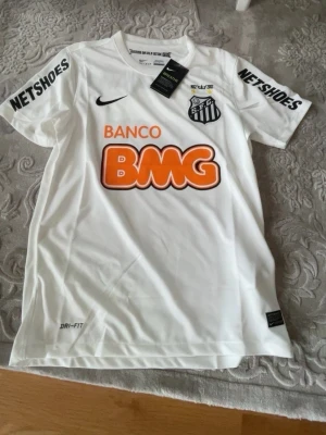 Vit Santos FC matchtröja Nike - (Pris kan diskuteras 300 var)                                   Säljer en vit Santos FC matchtröja från Nike med Dri-FIT-material. Tröjan har tryckta sponsorer som BMG och Netshoes samt klubbmärke på bröstet. Perfekt för dig som älskar brasiliansk fotboll och vill ha en snygg supportertröja.