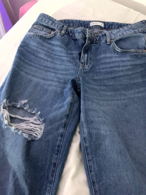 Blåa jeans med hål - Ett par blå jeans från Perfect Jeans med klassisk femficksmodell och ett stort slitet hål på vänster lår. Jeansen är baggy och sitter supper snyggt vid midjan 