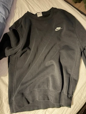 Svart sweatshirt från Nike - Klassisk svart sweatshirt från Nike med vit logga på bröstet. Tröjan har rund halsringning och långa ärmar. Perfekt för en avslappnad och sportig stil.