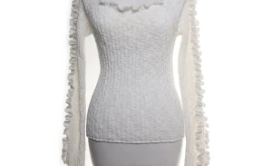 Vit stickad tröja med volangdetaljer - Trendig vit stickad tröja med figurnära passform och volangdetaljer längs den vida ringningen och ärmarna. Långärmad modell i mjukt material som ger en feminin och stilren look. Perfekt för dig som vill ha något extra till din outfit.