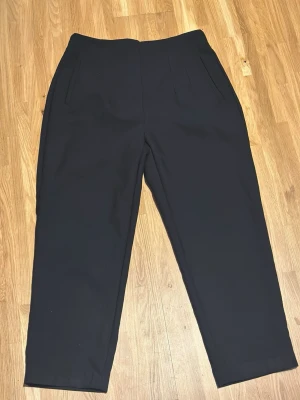 Svarta kostymbyxor från Zara XL - Stilrena svarta kostymbyxor från Zara i storlek XL. Byxorna har raka ben, två fickor fram och är tillverkade i ett mjukt, vävt material. Perfekta för en clean och klassisk look.