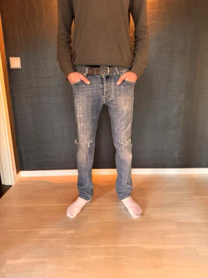 Blå slitna jeans från Jacob cohen - Säljer ett par blå jeans från Jacob Cohen med slitningar på knäna och klassisk femficksmodell. Jeansen har en rak passform och tydliga tvättade detaljer för en avslappnad look. Perfekta för dig som gillar en lite ruffare stil.