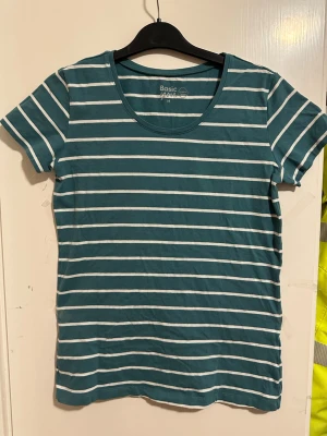 Randig grön t-shirt från Basic You strl: M - Snygg randig t-shirt från Basic You i en grön nyans med vita horisontella ränder. Tillverkad i mjuk ekologisk bomull och har en klassisk rund halsringning samt korta ärmar. Perfekt för en avslappnad och stilren look.