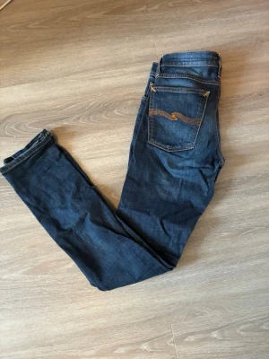 Mörkblå jeans från Nudie Jeans - Snygga mörkblå jeans från Nudie Jeans med klassisk femficksdesign och orangea kontrastsömmar. Jeansen har en smal passform och är tillverkade i denim av bomull. Bara skriva om ni har frågor🙌🏼