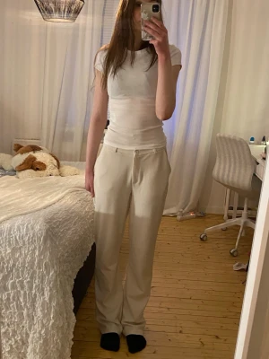 Beiga byxor med dragsko - Säljer ett par beige byxor med raka ben och dragsko i midjan. Byxorna har en enkel design och är tillverkade i ett mjukt material som passar perfekt för chill dagar. Perfekt för dig som gillar en avslappnad och stilren look.