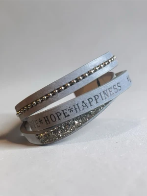 Grått wrap-armband från Lene Idar - Snyggt grått wrap-armband från Lene Idar med texten *LOVE*HOPE*HAPPINESS*. Armbandet har silverfärgade pärlor och glittrande stenar på ena bandet. Perfekt accessoar för att lyfta din stil.