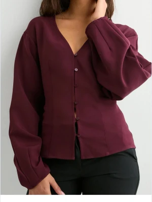 Vinröd blus med knappar och v-ringning - Andvänd en gång, säljer då den inte satt som jag hade önska! Stilren vinröd blus med v-ringning och knäppning framtill. Blusen har långa, löst sittande ärmar och markerad midja för en snygg siluett. Tillverkad i ett mjukt, vävt material som ger en elegant känsla. Perfekt att matcha med både jeans och kostymbyxor.🥰