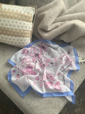 Blommig scarf  - Snygg sjal i vitt med rosa blommönster och ljusblå kant. Sval och tunn, perfekt att knyta runt halsen eller i håret. Fyrkantig form och mjukt, glansigt material som känns lyxigt. Den perfekta accessoarer för att liva upp outfiten och få in färg 💕