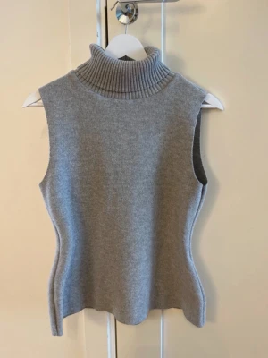 Grå ärmlös stickad poloväst - Snygg grå stickad väst med polokrage och ärmlös design. Perfekt att styla över en skjorta eller långärmad tröja. Mjuk och stretchig kvalitet som ger en clean och modern look.