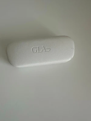 Vitt glasögonfodral från Glas - Snyggt och stilrent glasögonfodral i vitt konstläder från Glas. Fodralet har en mjuk, ljusrosa insida och präglad logga på ovansidan. Perfekt för att skydda dina glasögon i väskan eller fickan. Har nån liten bläck-stänk på ena sidan, se , bild, men är annars i jättebra skick. 