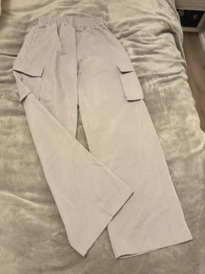 Beiga cargobyxor med fickor - Säljer ett par beiga cargobyxor med breda ben och stora sidofickor. Byxorna har resår i midjan för extra komfort och är tillverkade i ett lätt tyg, perfekt för en avslappnad stil. Inga synliga loggor eller märken.