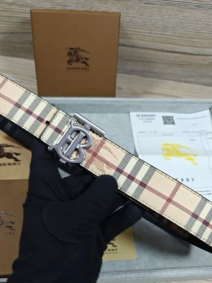 Burberry rutig bälte med silverdetalj - Säljer ett snyggt bälte från Burberry med klassiskt rutigt mönster i beige, svart och röd. Bältet har en stilren silverfärgad metallspänne med Burberrys ikoniska logotyp. Perfekt för att lyfta din outfit med en exklusiv touch.