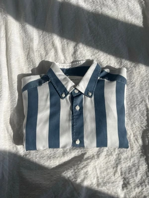 Blåvit randig skjorta med knappar - Snygg skjorta med breda blå och vita ränder och klassisk krage. Skjortan har knäppning framtill och vita knappar.