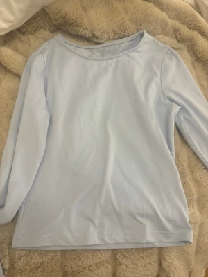 Ljusblå långärmad topp - En stilren ljusblå långärmad topp med rund halsringning. Enkel och clean design som passar perfekt till jeans eller kjol. Tillverkad i mjukt material för en bekväm känsla hela dagen. Har en svart fläck på baksidan. 
