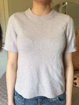Ljuslila stickad topp med kort ärm - Säljer en ljuslila stickad topp med rund hals och korta ärmar. Toppen har en enkel, clean design och är mjuk och bekväm att bära. Perfekt till jeans eller kjol för en avslappnad look. I 100% Kashmir 
