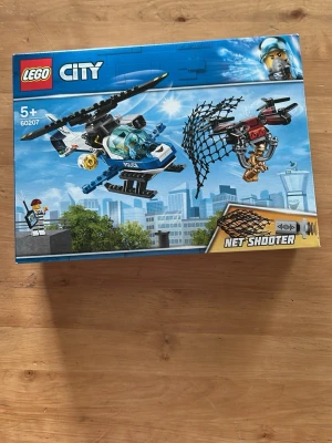 LEGO City Polishelikopter  - Säljer ett LEGO City set med polishelikopter och drönare, modell 60207. Setet innehåller en blå och vit helikopter, en röd och svart drönare samt minifigurer och tillbehör som nätkastare. Perfekt för dig som gillar action och byggleksaker.