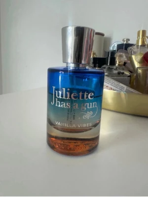 Juliette Has a Gun Vanilla Vibes EdP - Parfymen Vanilla Vibes från Juliette Has a Gun kommer i en snygg flaska med blå och kopparfärgad toning samt silverfärgat lock. Doften är en Eau de Parfum och flaskan rymmer 50 ml. Förpackningen är vit med elegant svart och röd text.