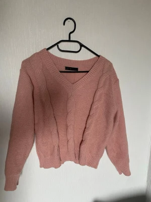 Rosa kabelstickad tröja V-ringad - Mysig kabelstickad tröja i dammig rosa med V-ringning och breda muddar. Tröjan har ett chunky mönster över hela tröjan