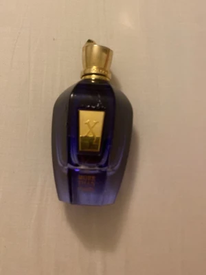 Xerjoff More Than Words parfym - Lyxig parfymflaska från Xerjoff i mörkblått glas med gulddetaljer och elegant guldlock. Flaskan har en exklusiv design med en rektangulär guldetikett på framsidan. Perfekt för dig som gillar unika och exklusiva dofter. 