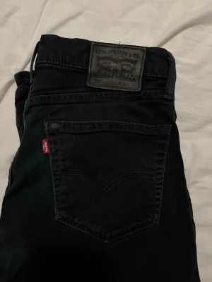 Svarta Levi's 511 jeans - Säljer ett par svarta Levi's 511 jeans med klassisk femficksdesign och rakt ben. Jeansen har en snygg svart tvätt, Levi's ikoniska röda etikett på bakfickan och patch i midjan. Perfekta för dig som gillar en tidlös och clean look.