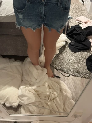 Blå jeansshorts med fransig kant - Säljer ett par klassiska blå jeansshorts med fransig, rå kant och femficksmodell. Shortsen har normal passform och stängs med knapp och dragkedja. Perfekta för sommaren och ger en avslappnad look.