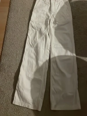 Vita raka jeans med stora fickor - Säljer ett par vita jeans med raka ben och stora fickor både fram och bak. Jeansen har hög midja och är tillverkade i ett kraftigare bomullstyg. Perfekta för dig som gillar en clean och avslappnad stil.