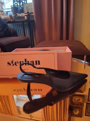 Svarta spetsiga pumps - Säljer ett par eleganta svarta pumps från Stephan Paris. Skorna har spetsig tå, låg klack och öppen häl med elastisk rem. Tillverkade i ett slätt material som ger en stilren look. Perfekta för dig som vill ha en klassisk och trendig sko.