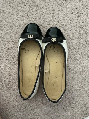 Svarta och vita ballerinaskor med rosett - Snygga ballerinaskor i svart och vitt med lackad tå och dekorativ rosett framtill. Storlek 38🩷