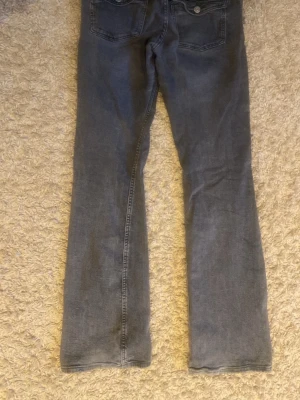 Grå bootcut jeans med fem fickor - Snygga grå jeans med bootcut passform och klassisk femficksdesign. Jeansen har låg midja och dragkedja med knapp framtill. Perfekta för en avslappnad och trendig look.