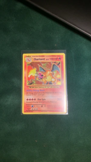 Charizard Pokémonkort Holo - Säljer ett Charizard Pokémonkort med holografisk effekt. Kortet har en färgstark design med Charizard i orange och blått, samt detaljer i rött och gult. Kortet är inplastat i ett skyddsfodral och är perfekt för samlare eller Pokémonfans. För fler bilde där det bara att skriva