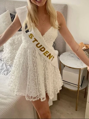 Vit spetsklänning med omlott - Superfin vit kort klänning med omlott och spetsdetaljer. Klänningen har v-ringad hals och är ärmlös med tunna axelband. Perfekt för student eller sommarens alla tillfällen. Materialet är lätt och luftigt❤️endast använd en gång på min själva student mottagning❤️