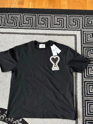 Svart t-shirt från AMI Paris med hjärtdetalj - Svart t-shirt från AMI Paris med en stor broderad hjärtdetalj på bröstet. Klassisk rund halsringning och korta ärmar. Tillverkad i mjuk bomull för en skön känsla och stilren look.