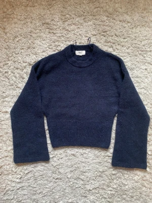 Mörkblå stickad tröja Gina Tricot - Mysig mörkblå stickad tröja från Gina Tricot i ullblandning. Tröjan har en croppad passform, långa ärmar och rund halsringning. Perfekt för lager-på-lager och en stilren look. Endast använd en gång!