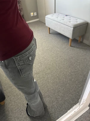 Gråa bootcut jeans med fickdetaljer - Säljer ett par gråa bootcut jeans med snygga fickdetaljer och silverknappar. Jeansen har klassisk femficksdesign och är tillverkade i ett mjukt denimtyg. Perfekta för en avslappnad och trendig look.