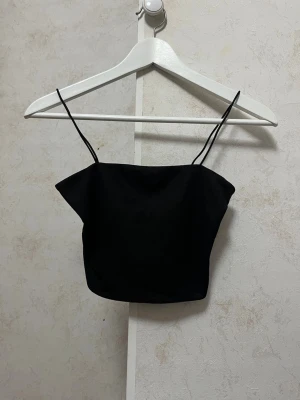 Svart linnetopp med tunna axelband - En basic svart linnetopp med tunna axelband och rak skärning. Toppen är ärmlös och har en croppad passform som passar perfekt till jeans eller kjol. Enkel och snygg design som är lätt att matcha med olika outfits.