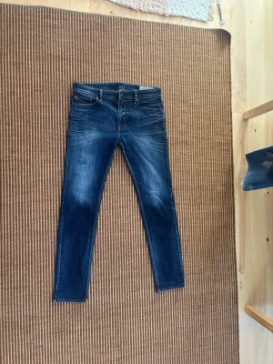 Mörkblå slim fit jeans - Snygga mörkblå slim fit jeans med slitningar och tvättade detaljer. Klassisk femficksmodell med dragkedja och knapp framtill. Jeansen har en modern passform och är perfekta för en trendig look.