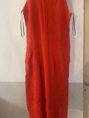 Röd ribbad långklänning från H&M - Cool röd långklänning från H&M med ribbad struktur och svarta snörningsdetaljer vid axlarna. Klänningen har en rak och loose passform som ger en avslappnad vibe. Perfekt för dig som vill sticka ut med färg och enkel design.