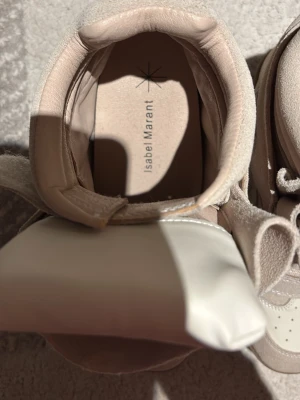 Beige sneakers från Isabel Marant - Snygga beige sneakers från Isabel Marant med högt skaft och breda kardborreband. Skorna har en mix av mocka och läderdetaljer samt perforerad tå för extra stil. Perfekta för dig som gillar trendiga och bekväma skor med unik design.