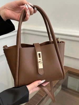 Brun handväska med gulddetalj - Snygg brun handväska i slätt konstläder med stilren guldfärgad låsdetalj framtill. Väskan har dubbla handtag och en avtagbar axelrem för flexibel användning. Perfekt storlek för det viktigaste och en modern, minimalistisk look.