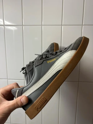 Puma sneakers - Stilrena och väldigt snygga Puma sneakers i mörkgrå färg med vit Puma-strip och klassisk gum-sula. Skorna endast använda en gång och i fint skick utan något slitage.  Perfekta både till vardags och för en clean streetwear-look. Bekväma på foten och lätta att matcha med nästan vilken outfit som helst.