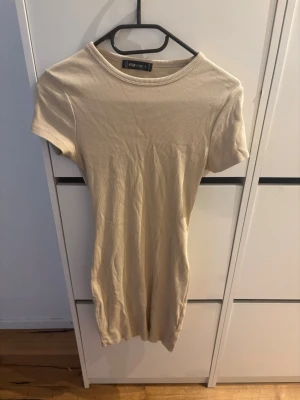 Beige ribbad kortklänning från FB Sister - En beige ribbad kortklänning från FB Sister med rund halsringning och korta ärmar. Klänningen har en slim passform och är tillverkad i ett mjukt, stretchigt material som sitter snyggt på kroppen. Perfekt för en enkel och stilren look.