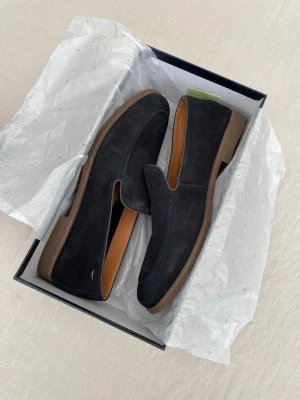 Mörkblå mocka loafers - Stilrena mörkblå loafers i mocka från Mango med klassisk design och bruna sulor. Skorna har en mjuk insida i ljust läder och passar perfekt till en dressad look. Snygga detaljer och enkel slip-on-modell.