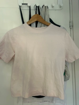 Ljusrosa t-shirt från Gina Tricot - En basic ljusrosa t-shirt från Gina Tricot, modell elevated basics. T-shirten har rund halsringning och korta ärmar, perfekt för en enkel och stilren look. Tillverkad i mjuk bomull som känns skön mot huden.