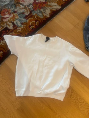 Vit sweatshirt från H&M - En stilren vit sweatshirt från H&M med klassisk rund halsringning och ribbade muddar. Tröjan är i mjukt bomullsmaterial och har en avslappnad passform, perfekt för en chill och enkel look.