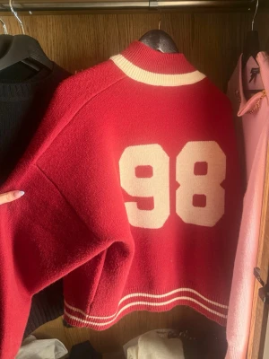 Röd collegekofta med siffran 98 - Trendig Edikted cardigan. Klassisk collegeinspirerad design med ribbade muddar och krage. 