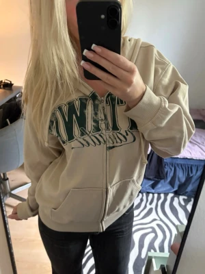 Zip-hoodie  - Beige zip-hoodie med stor grön text framtill. Den är från HM och aldrig använd💗 