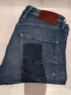 Blå jeans från Replay - Snygga blå jeans från Replay med klassisk femficksdesign och läderpatch bak i midjan. Jeansen har raka ben och coola detaljer på bakfickan. Perfekta till vardagsstilen och lätta att matcha med det mesta.