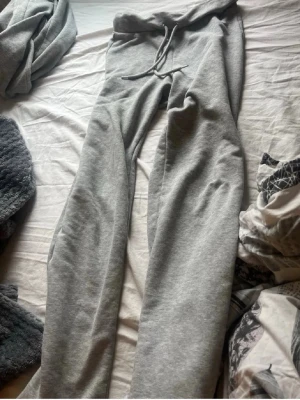 Grå mjukisbyxor med dragsko - Säljer ett par klassiska grå mjukisbyxor med dragsko i midjan och raka ben. Byxorna är i mjukt och bekvämt material, perfekta för chill dagar hemma eller när du vill vara extra comfy. Inga synliga loggor eller märken.